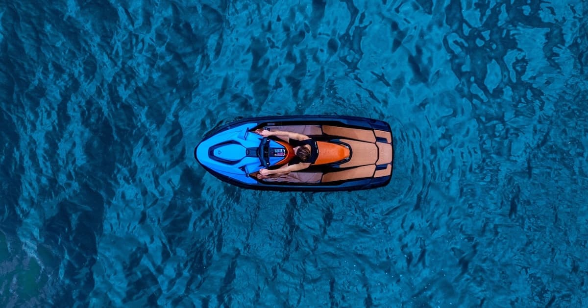 Top-down view of a person riding a blue-and-orange personal watercraft across textured blue water.