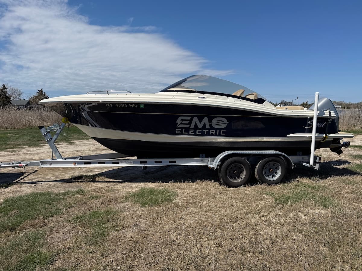 Scout Dorado 215 EMO electric boat on a dual-axle trailer in a grassy outdoor setting.