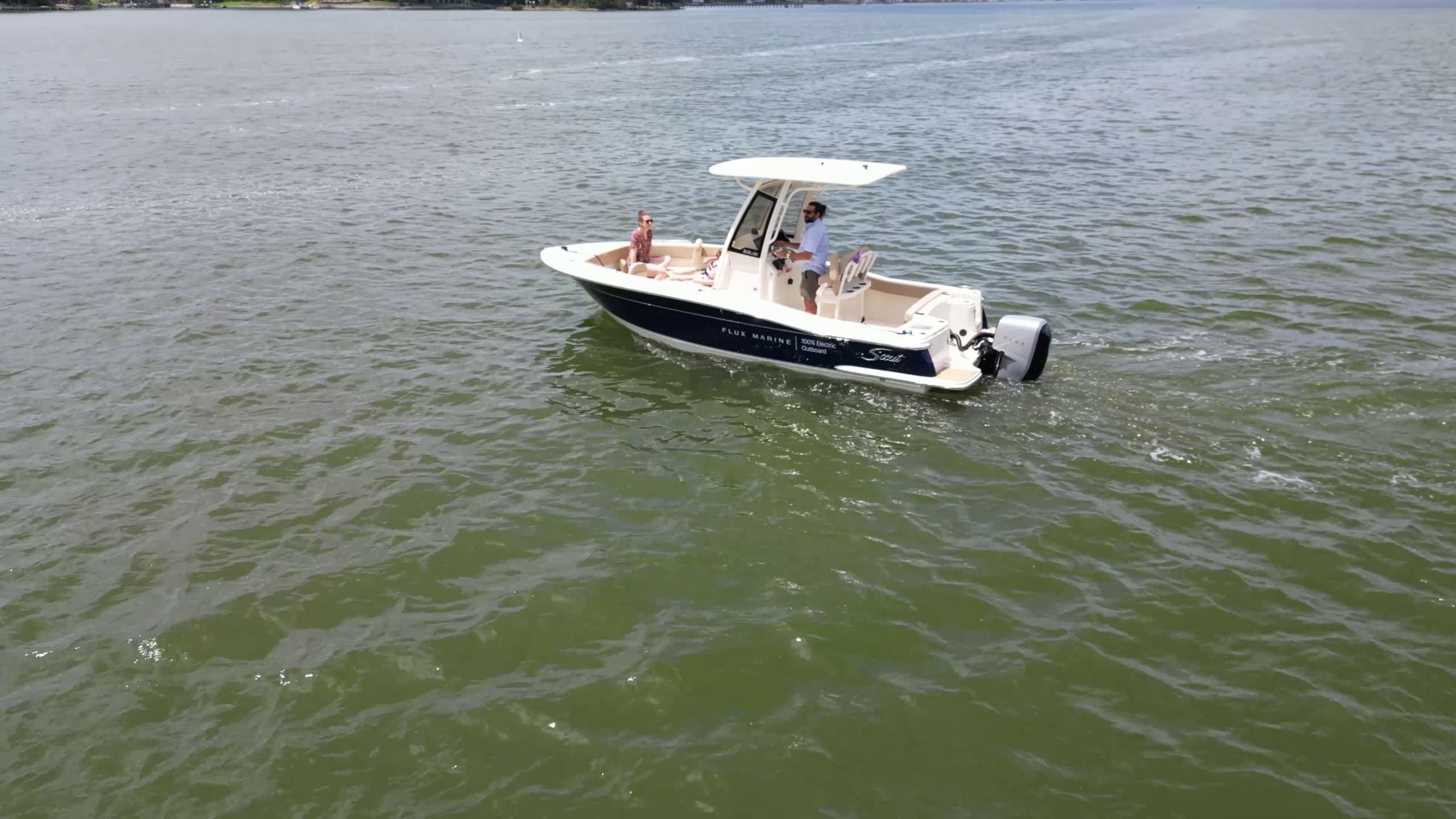 Scout 215 XSF center-console boat cruising on calm water with two people aboard and a white T-top.