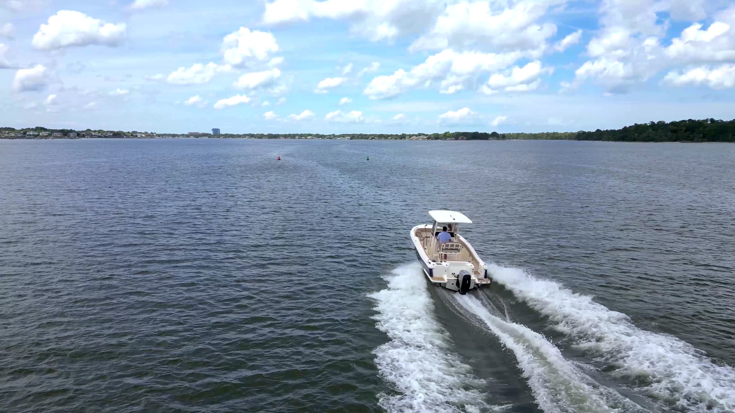 Scout 215 XSF center-console boat cruising across open water, leaving a white wake beneath a partly cloudy sky.
