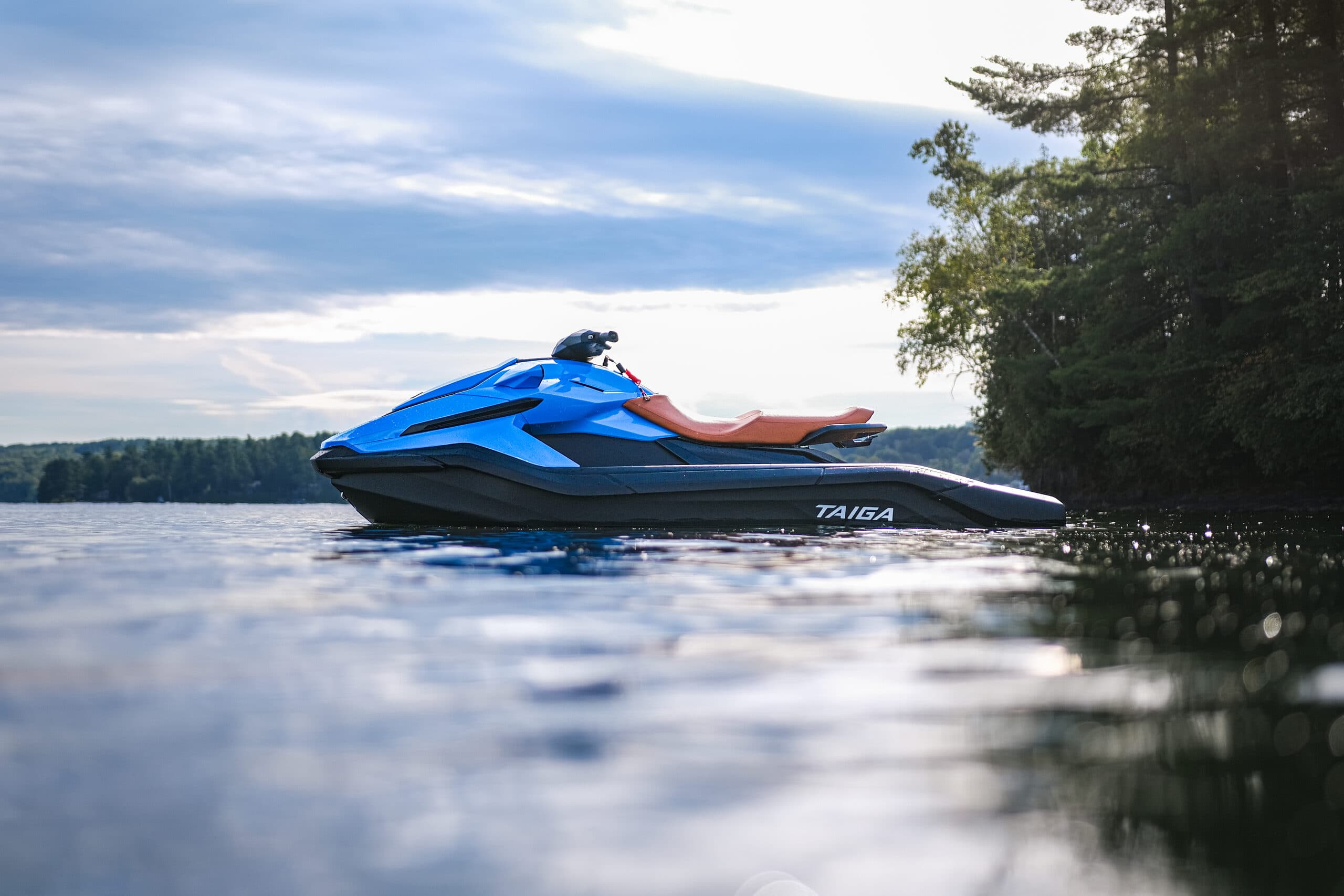 Blue Taiga Orca WX3 personal watercraft cruising on a calm lake near a tree-lined shore.
