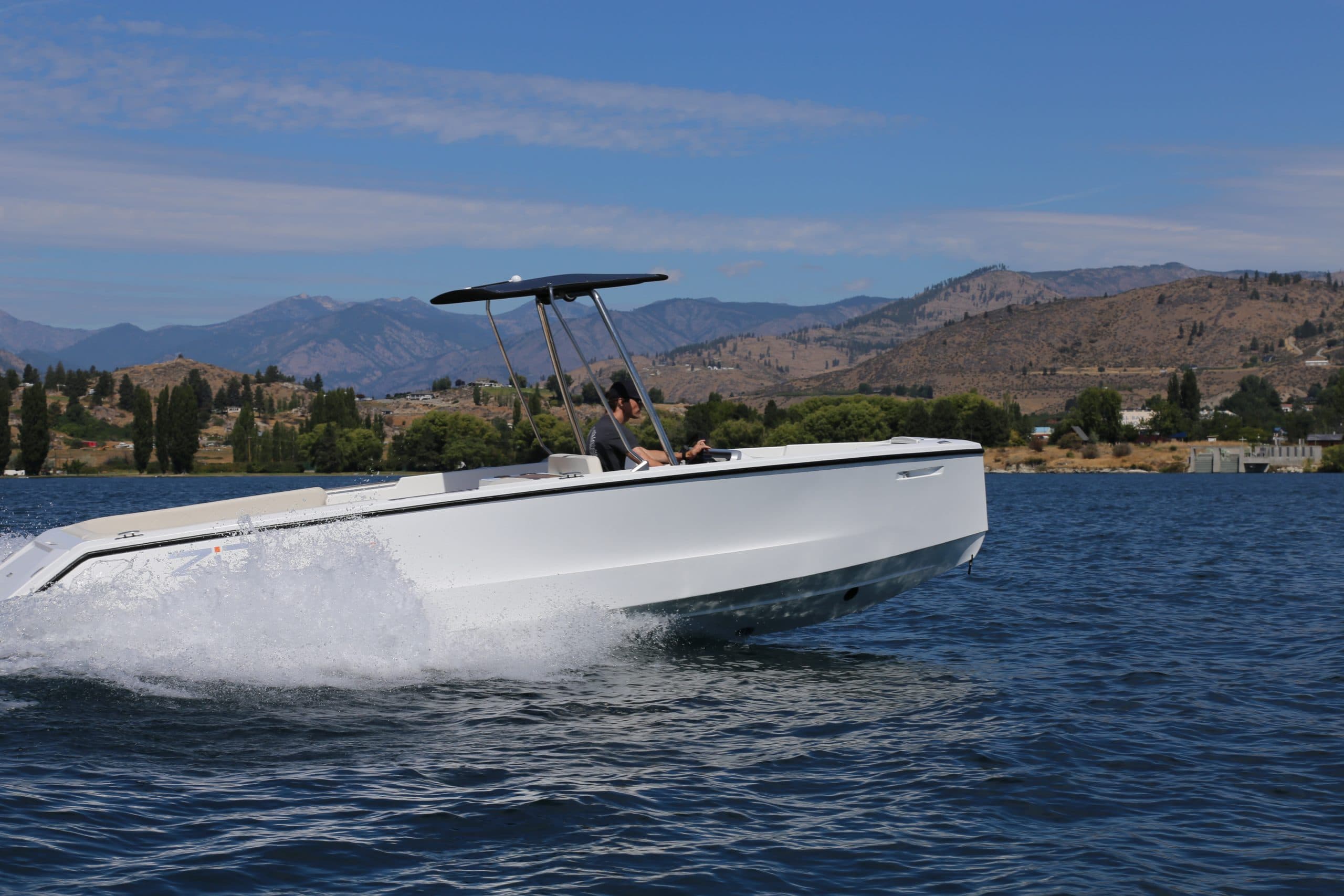 2026 Zin Boats Z7 electric center console boat on a lake with mountains and shoreline in the background.