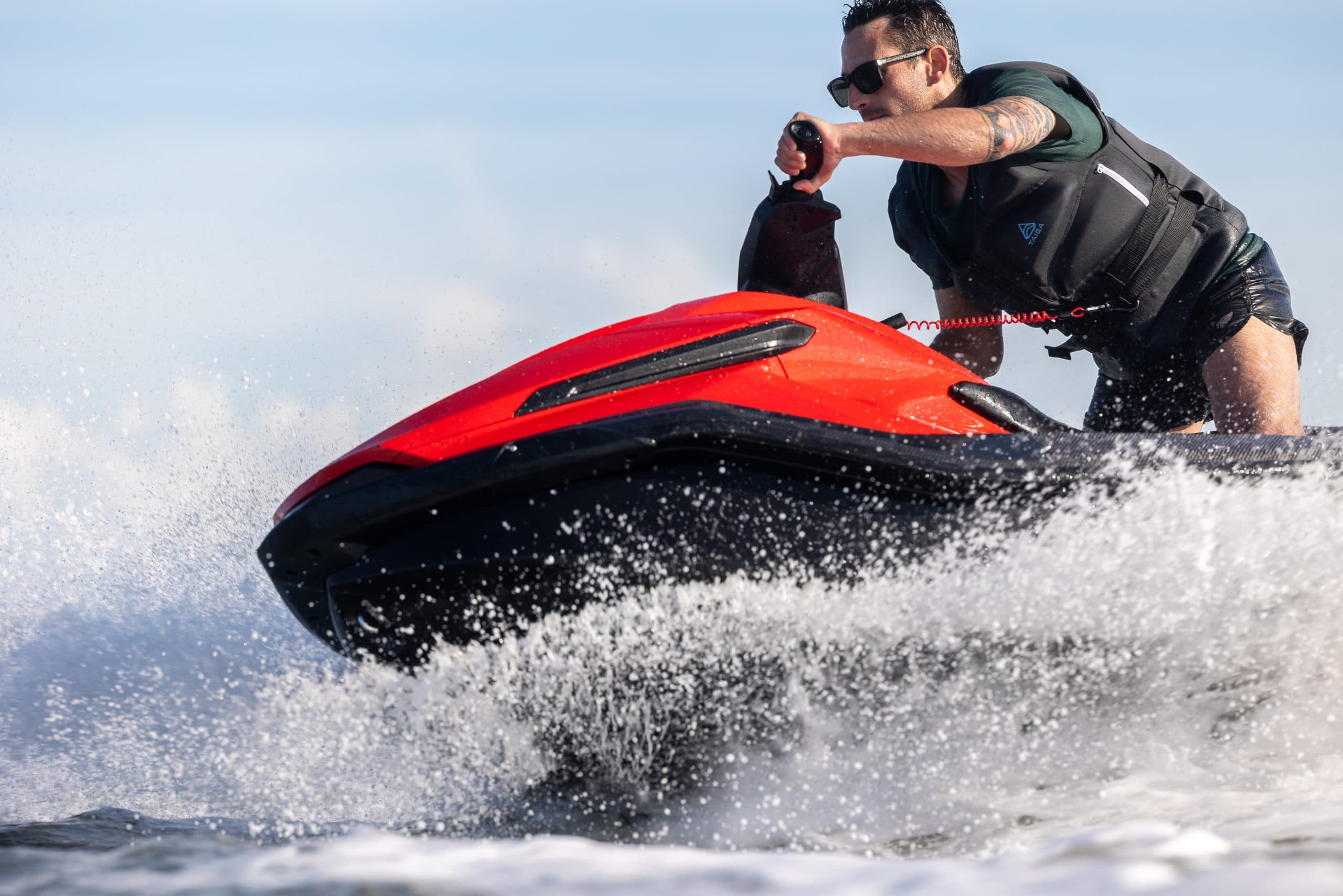 Rider operating a red-and-black Taiga Orca P2 electric personal watercraft across choppy water.