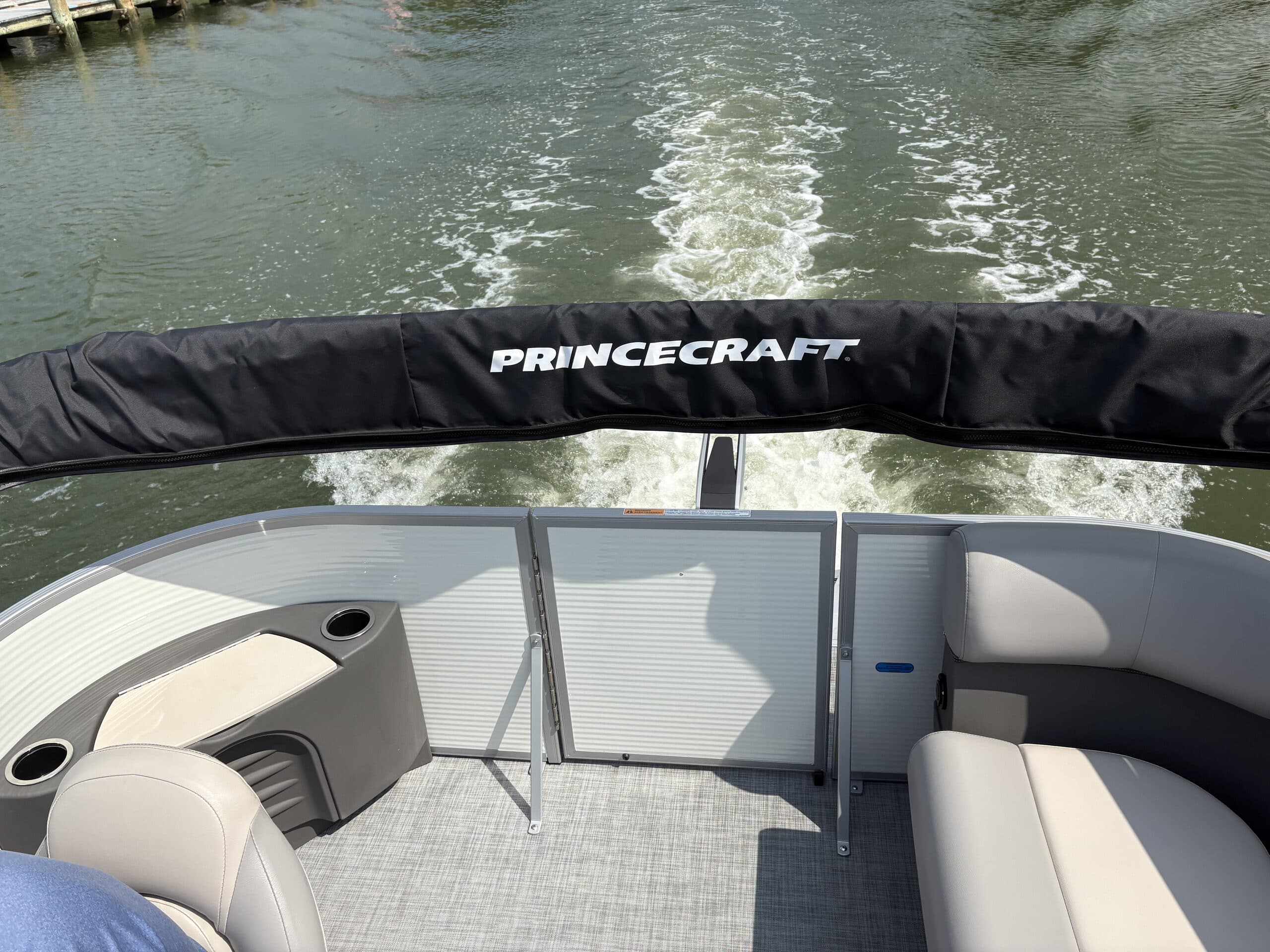 Interior of a Princecraft Brio E17 electric pontoon boat underway, showing bench seating, and black bimini top not deployed.
