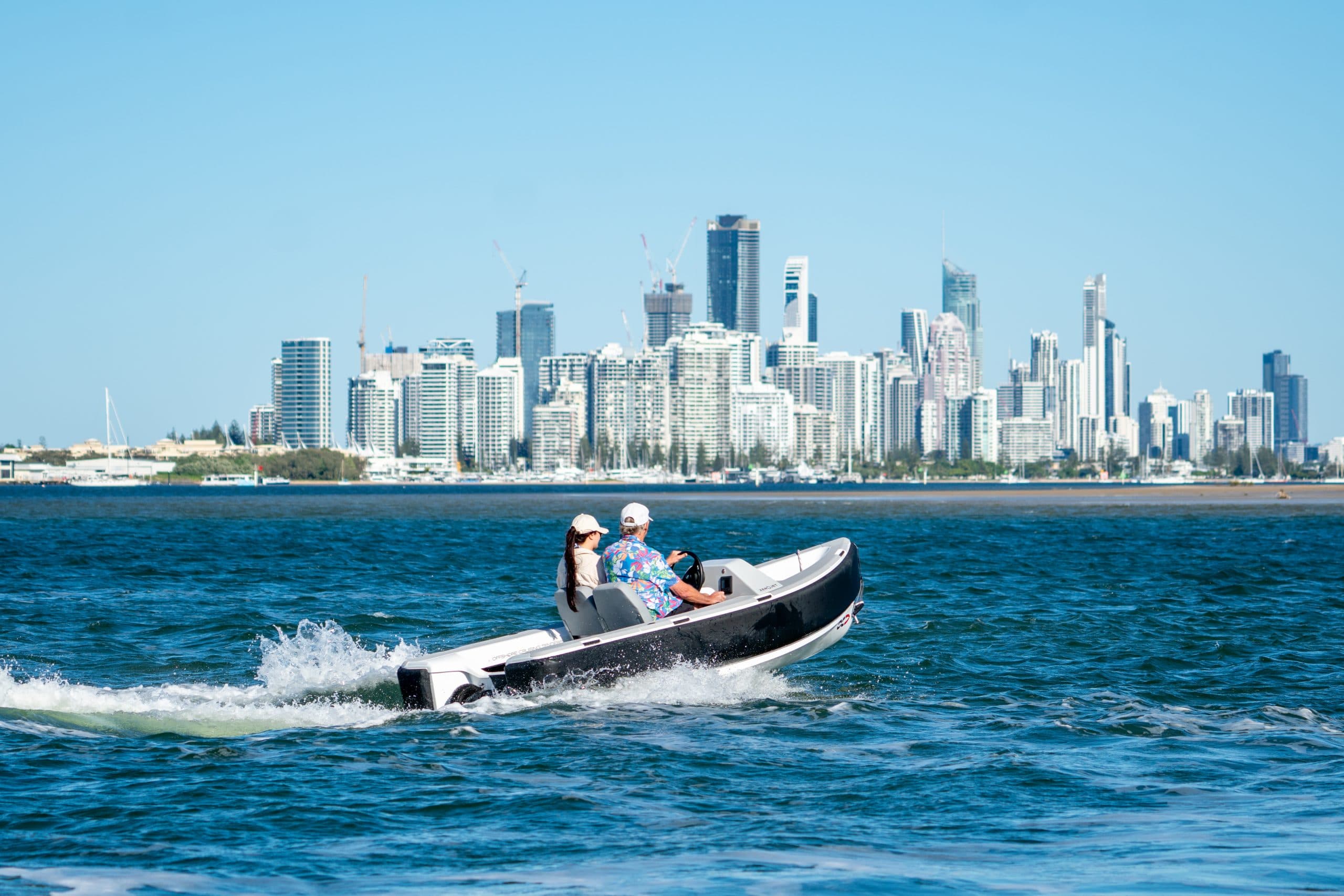 Two people in a white tender with a black rub rail and the city in the background